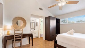 A hotel room with a bed, a desk with a chair, a large mirror, a wardrobe, and a ceiling fan.