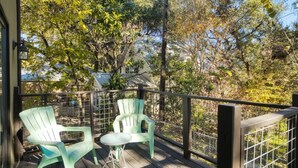 A wooden deck with two green chairs and a small table, surrounded by a metal railing. - Ravey #B xxxxxxxxxxx (Austin)
