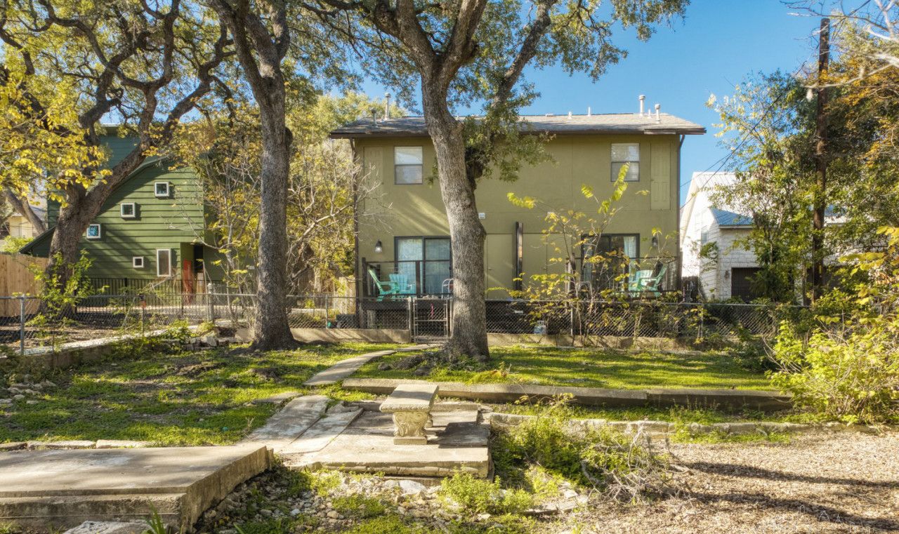 A residential area with a two-story house, a fenced yard, and a stone bench.