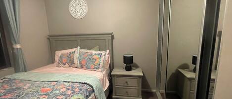 Un dormitorio con cama, mesitas de noche, lámpara, espejo y un adorno en la pared.