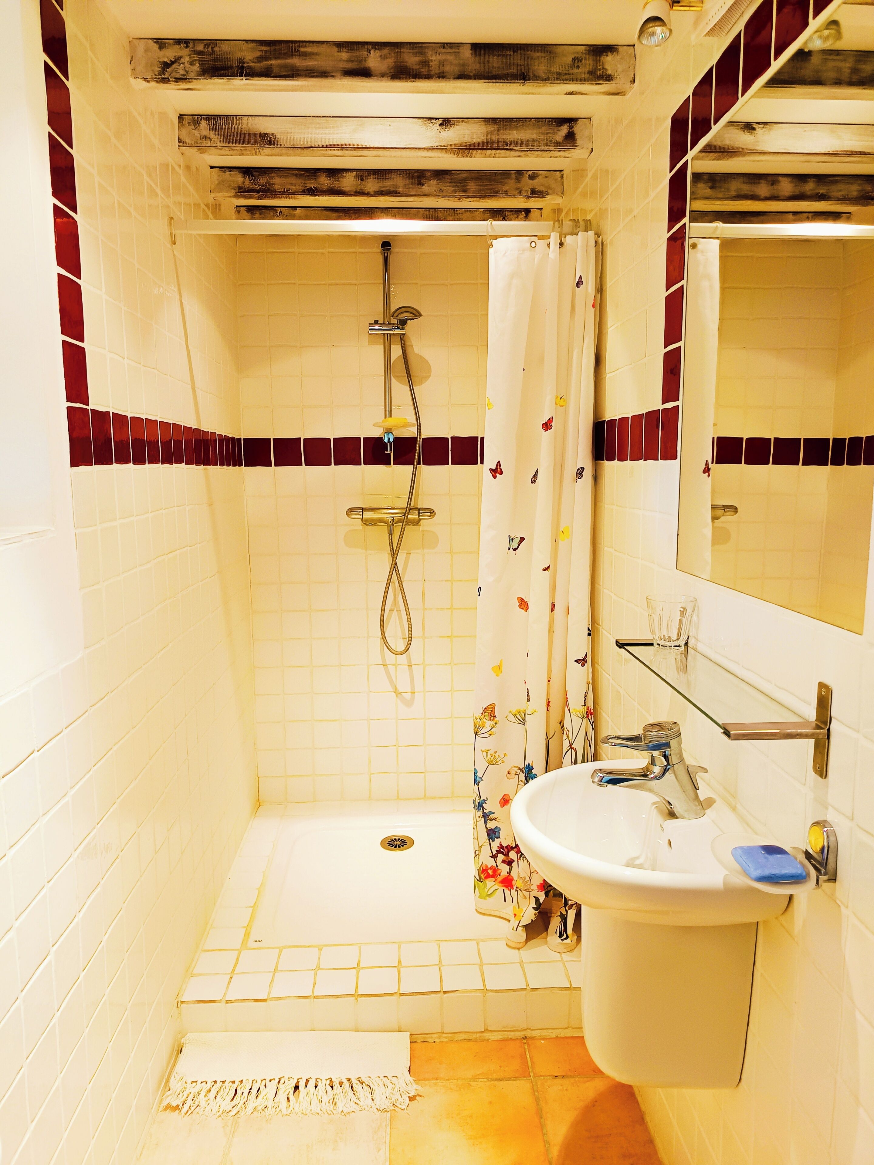 Et badeværelse med bruser, toilet, håndvask og spejl.