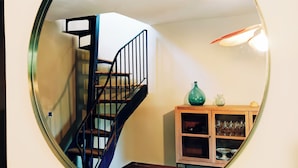 Un miroir rond reflétant un escalier, un meuble en bois contenant de la verrerie, et un vase vert.