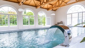 A swimming pool with a waterfall feature, large arched windows, and a wooden ceiling.