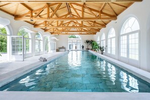 A large indoor swimming pool with clear water, surrounded by arched windows and wooden beams.