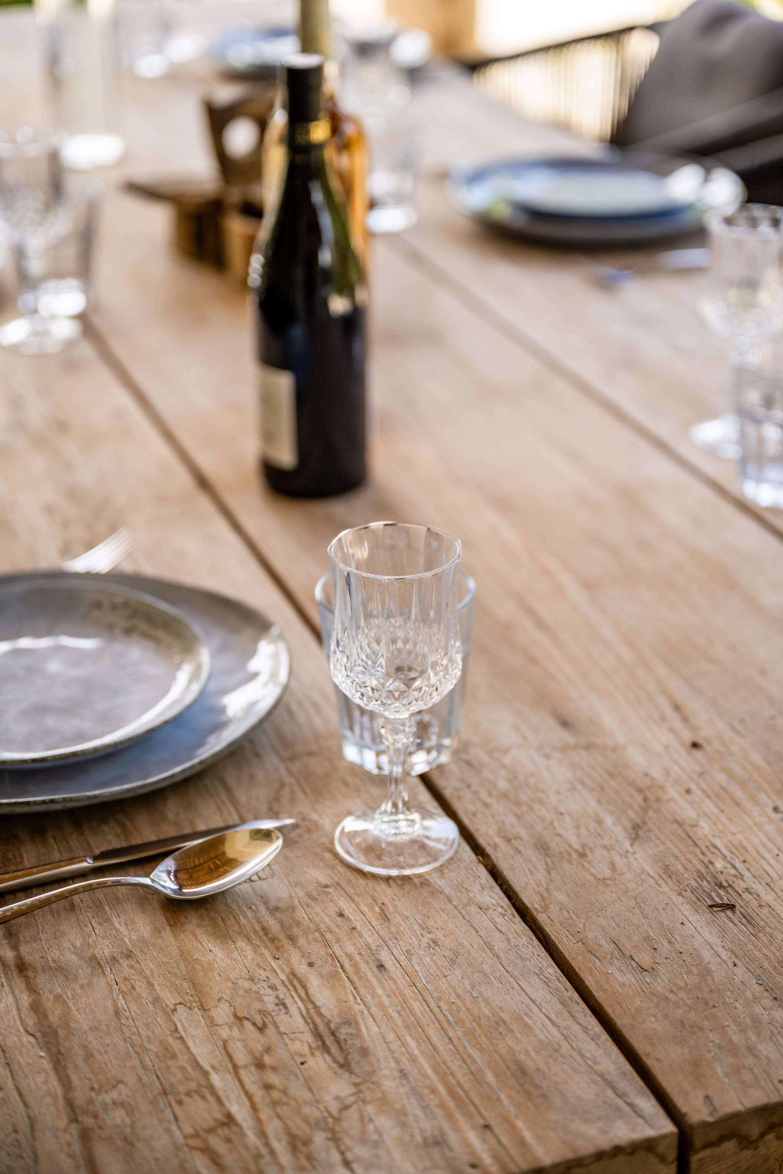 Ein Holztisch mit einer Weinflasche, einem Glas und Besteck.