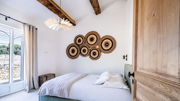 Een slaapkamer met een bed, kussens, een houten garderobe, een wandlamp en uitzicht door een raam.