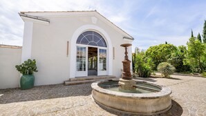 A building with a white facade, a stone courtyard, a fountain, and a potted plant.
