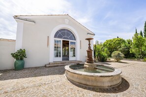 A building with a white facade, a stone courtyard, a fountain, and a potted plant.