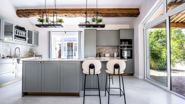 A modern kitchen with grey cabinets, a marble countertop, and a large island with bar stools.