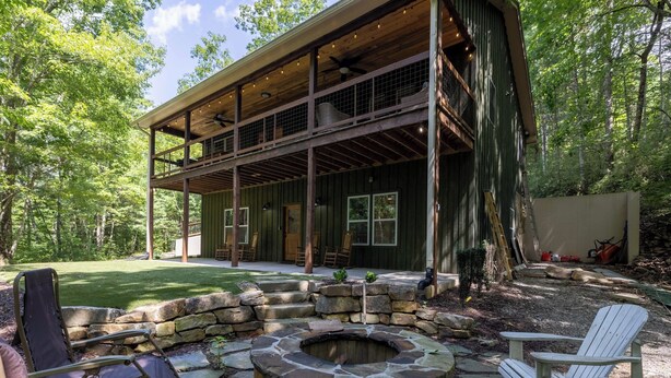 Un chalet rustique doté d’un foyer en pierre, de sièges d’extérieur et d’une véranda couverte.