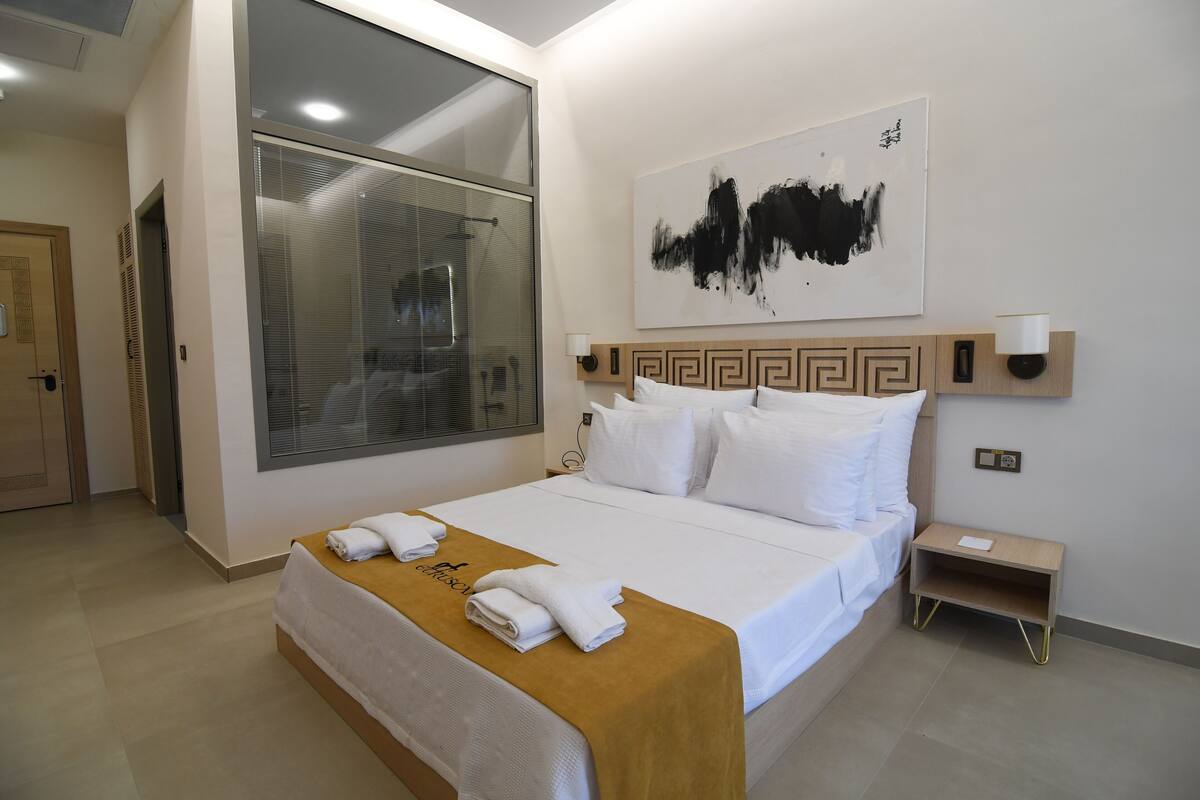 A hotel room with a large bed, a wooden headboard, a wall-mounted artwork, and a nightstand with a lamp.