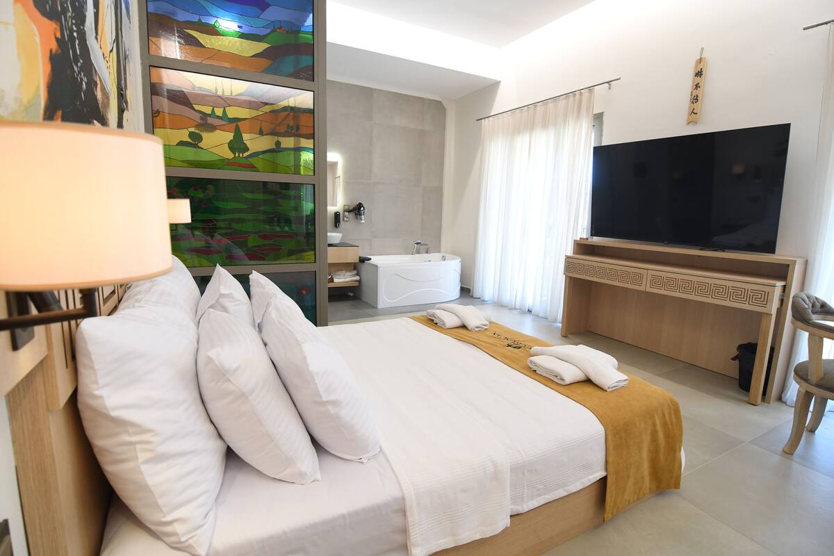 A hotel room with a bed, a TV, a bathroom, and a painting on the wall.