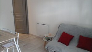 A room with a wooden dining table, white chairs, a grey sofa with red cushions, and a small round table with a candle.
