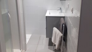 A modern bathroom with a glass shower enclosure, a white sink, and a towel rack.