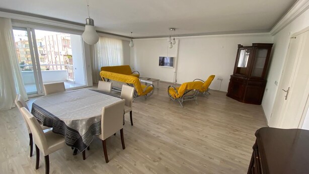 Un salon spacieux comprenant une table à manger, deux fauteuils jaunes et un téléviseur fixé au mur.