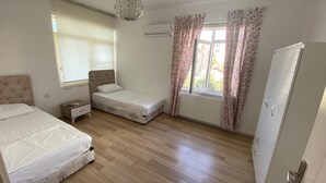 Een slaapkamer met twee bedden, een kledingkast, een radiator en een raam met bloemen gordijnen.