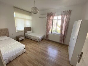 Une chambre avec deux lits, une armoire, un radiateur et une fenêtre ornée de rideaux à motifs floraux.