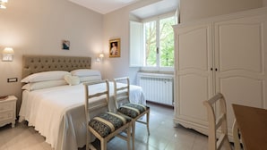 A bedroom with a bed, two chairs, a table, a wardrobe, and a window with a view of trees. - Exclusive  apartment in Perugia centre with parking  (perugia)