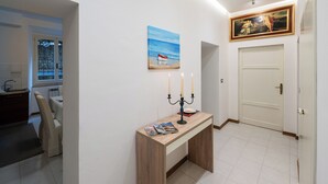 A hallway with a wooden console table, a painting of a boat on the sea, a door, and a tiled floor. - Exclusive  apartment in Perugia centre with parking  (perugia)