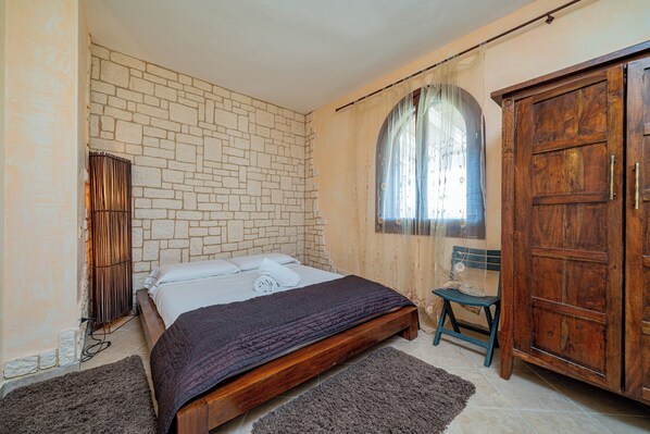 A bedroom with a stone wall, a wooden bed, a chair, and a wardrobe. - Casa Hermes by Wonderful Italy (Olbia)