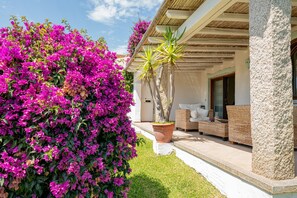 A well-maintained garden with vibrant bougainvillea flowers, a wicker sofa, and a stone pillar. - Casa Hermes by Wonderful Italy (Olbia)