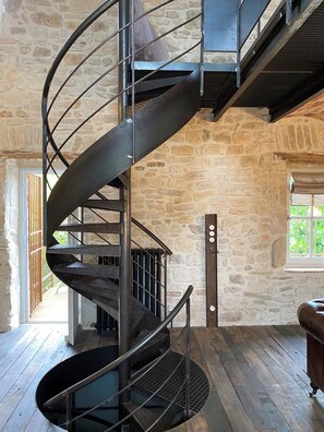 A spiral staircase with metal railings in a room with stone walls and wooden flooring.