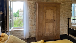 A room with stone walls, a wooden wardrobe, a bed with yellow bedding, and a window with curtains.