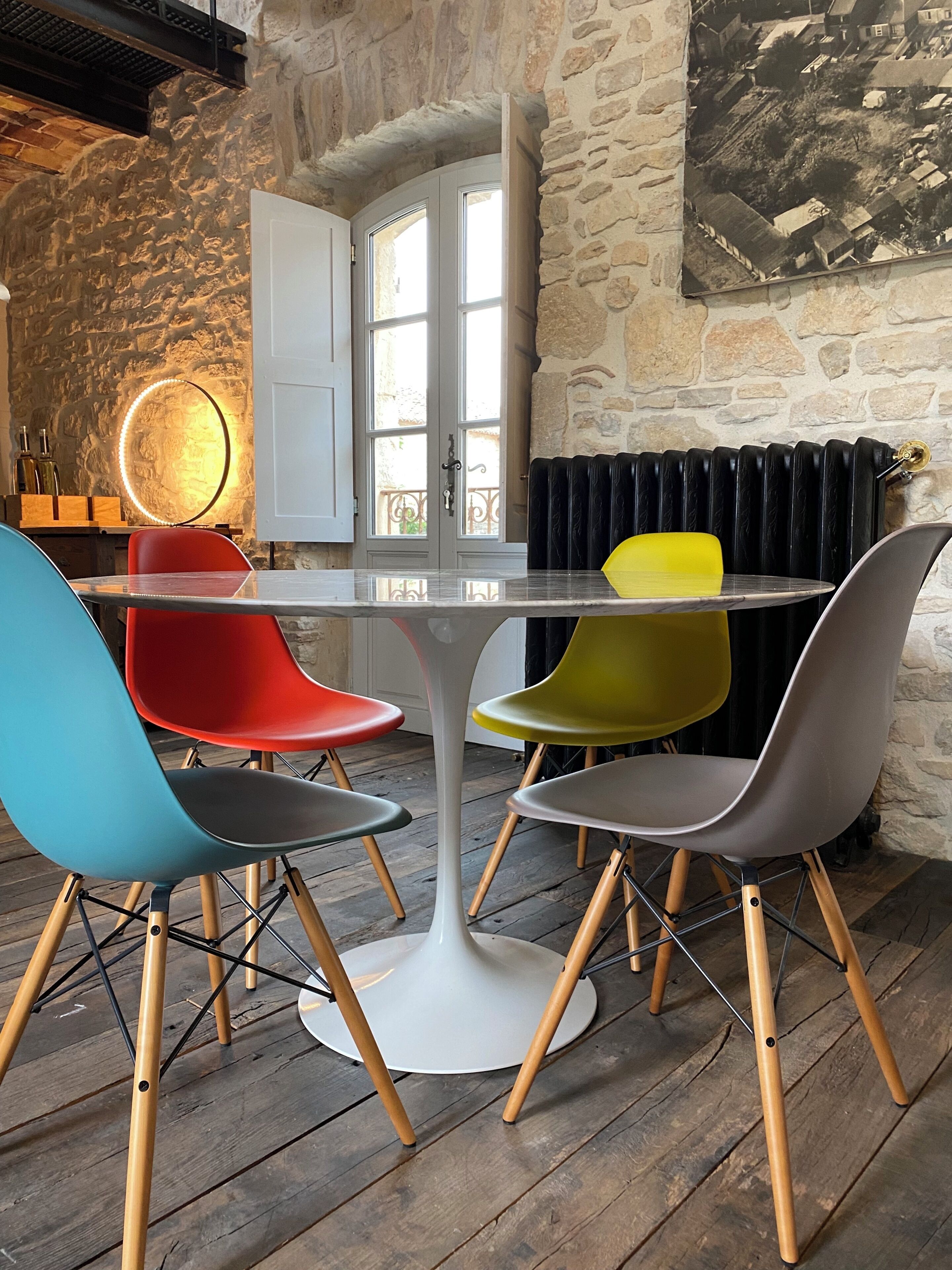 Une table ronde dotée d’un pied central blanc, entourée de quatre chaises aux pieds en bois et aux structures métalliques.