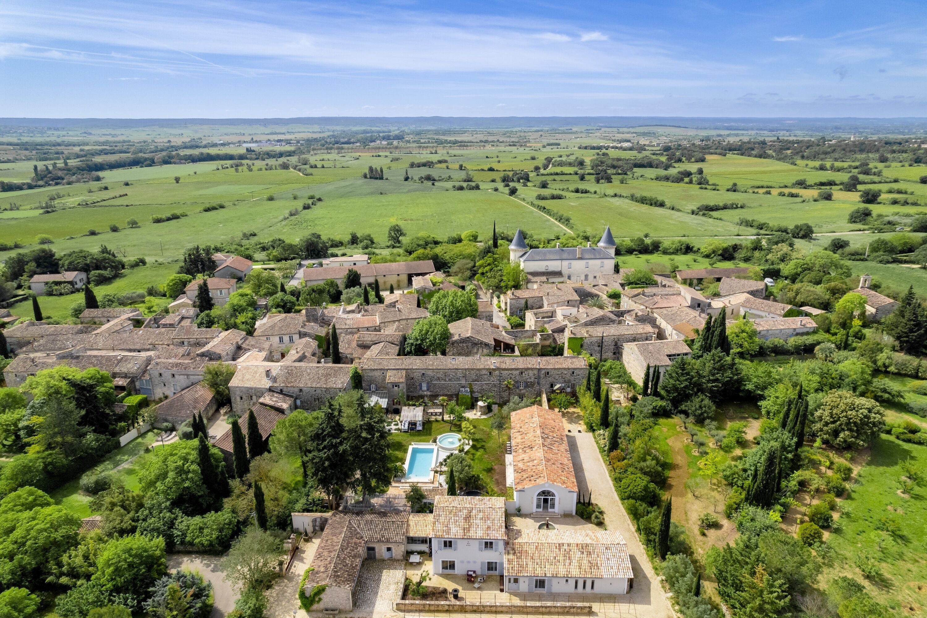 A historic village with traditional stone buildings, a central courtyard, and a large open field in the background.