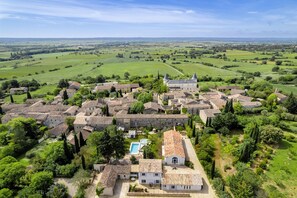 A historic village with traditional stone buildings, a central courtyard, and a large open field in the background.