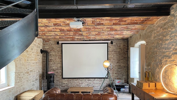 A room with a leather sofa, a projector screen, and a wooden desk with a lamp.