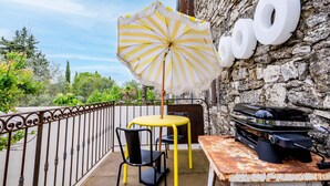 A patio with a yellow table and chairs, a striped umbrella, and a barbecue grill against a stone wall.