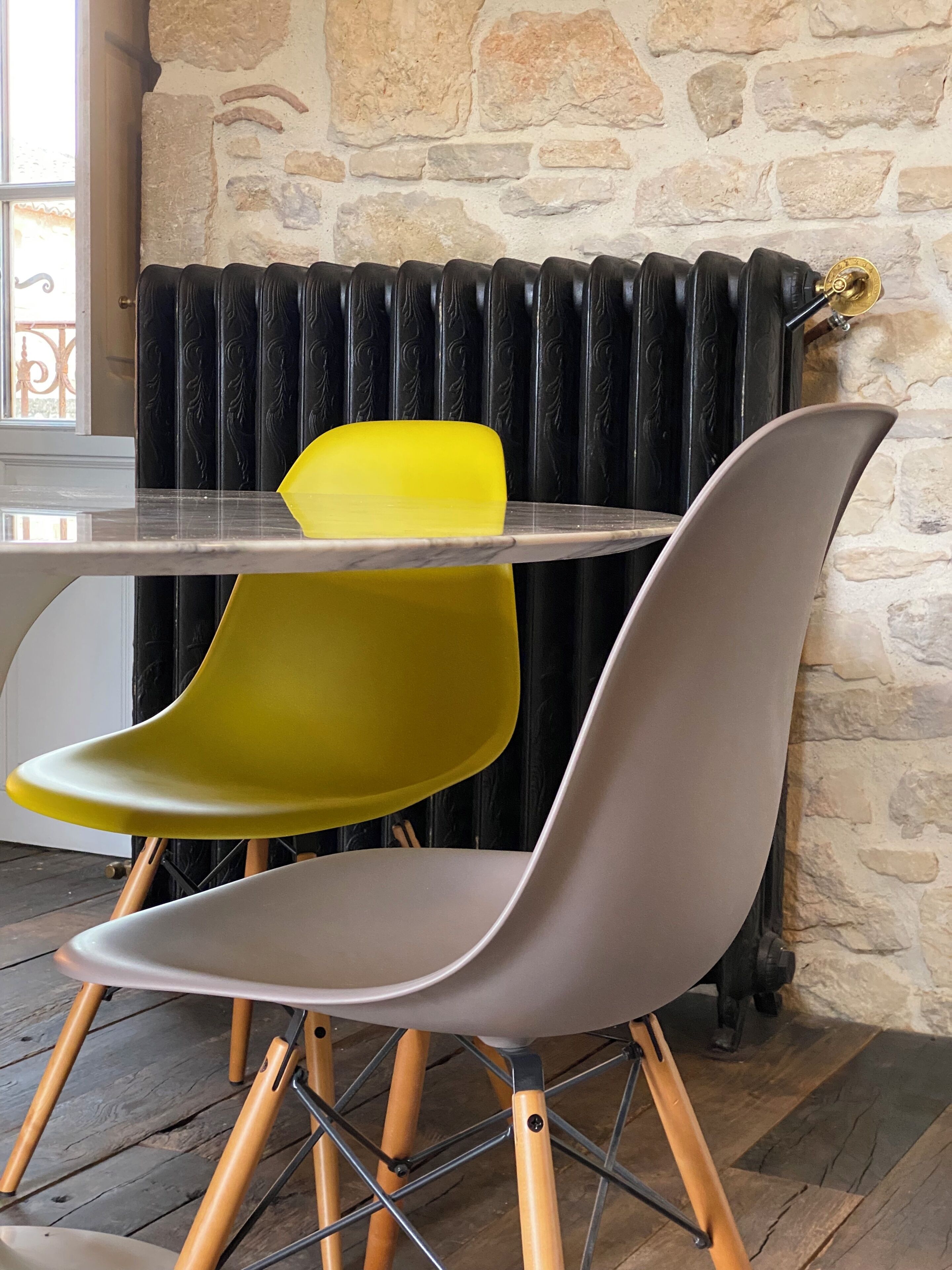 Een eethoek met een stenen muur, een radiator en twee stoelen met houten poten.