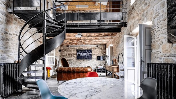 A modern interior with a spiral staircase, a round marble table, and a leather sofa.