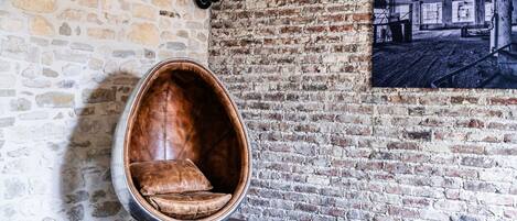 A room with exposed brick walls, a hanging chair, a wooden table with a game, and a leather ottoman.