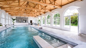 A large indoor swimming pool with a wooden ceiling and arched windows.