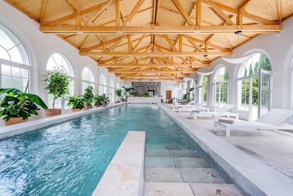 A large indoor swimming pool with a wooden ceiling and arched windows.