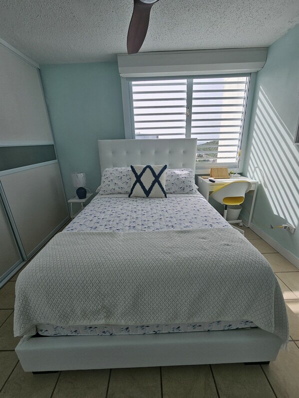 Une chambre à coucher avec un lit, un bureau et une fenêtre équipée de stores.