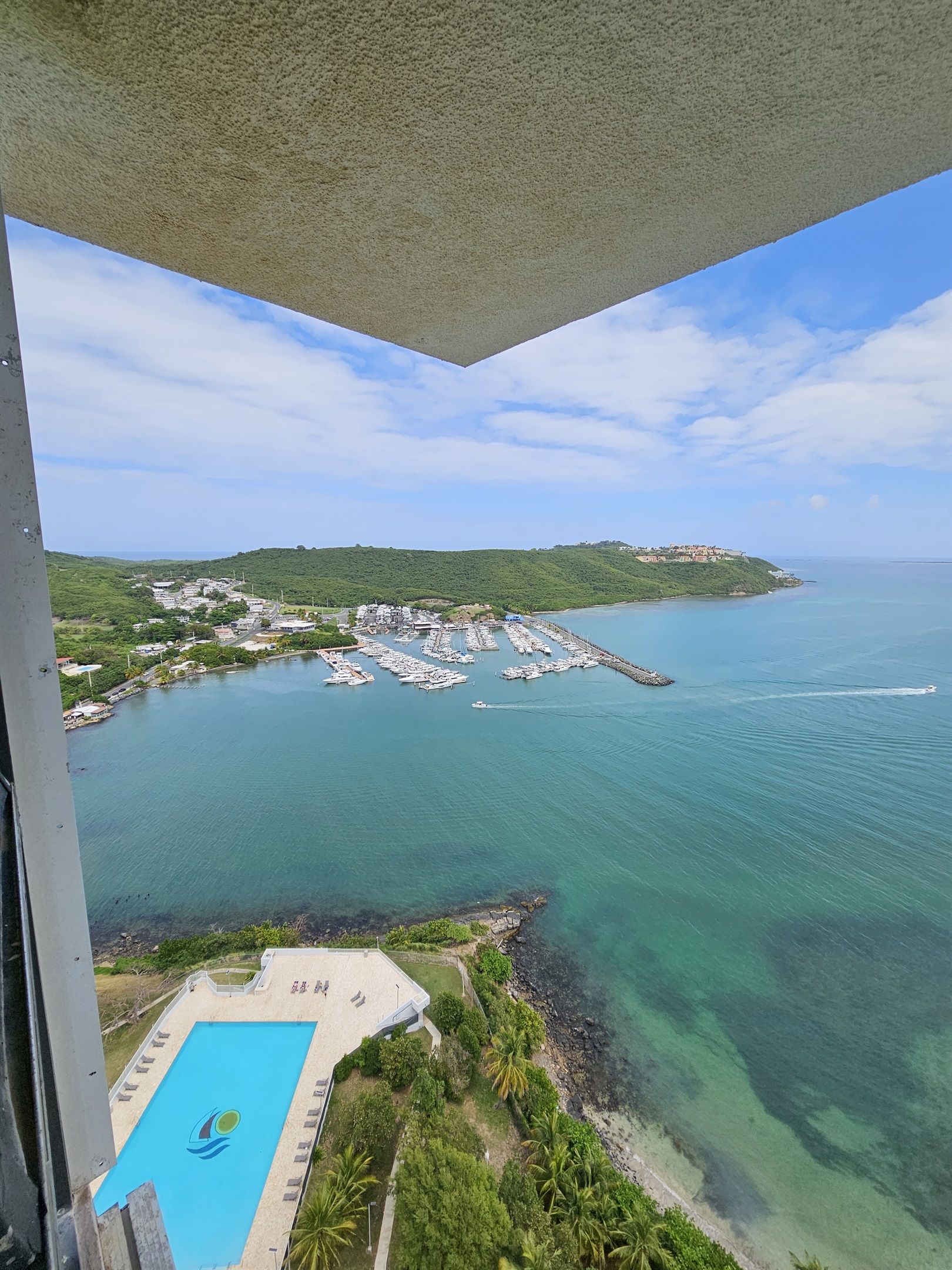 Vista de un puerto deportivo con barcos, piscina y paisaje costero.
