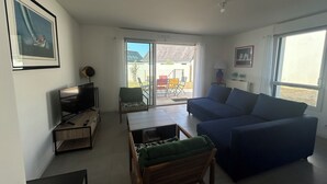 A living room with a TV, sofa, and a chair. There's a sliding glass door leading to a patio area with outdoor furniture. - New apartment for 4 people in Arzon (Arzon)