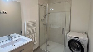 A modern bathroom with a glass-enclosed shower, a built-in washing machine, and a vanity with a mirror. - New apartment for 4 people in Arzon (Arzon)