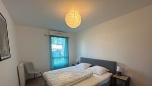 A bedroom with a bed, bedside tables, a chair, a radiator, and a window with curtains. - New apartment for 4 people in Arzon (Arzon)