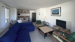 A modern living room with a blue sofa, a small TV, and a dining area with a table and chairs. - New apartment for 4 people in Arzon (Arzon)