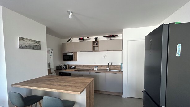 A modern kitchen with a wooden island, two bar stools, a black refrigerator, and a microwave. - New apartment for 4 people in Arzon (Arzon)