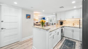 Una cocina moderna con armarios blancos, encimeras de granito y una isla central.