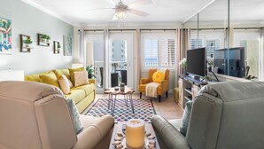 A living room with a sofa, armchairs, a coffee table, a TV, and a ceiling fan. - 410- Newly added 2 BR/ 2 BA Condominium with Free Beach Service! (Destin)
