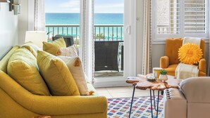 A living room with a yellow sofa, a small table with a plant, and a view of the ocean through a sliding door. - 410- Newly added 2 BR/ 2 BA Condominium with Free Beach Service! (Destin)