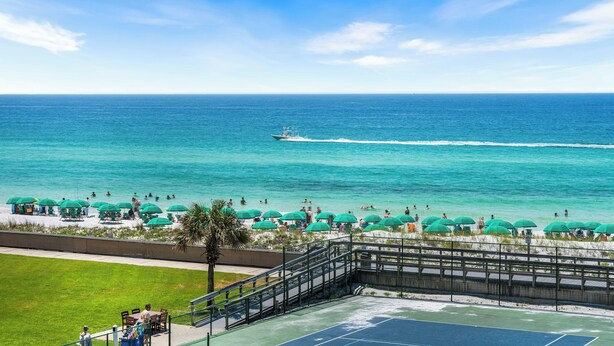 A beach view with a tennis court, umbrellas, and people swimming. - 410- Newly added 2 BR/ 2 BA Condominium with Free Beach Service! (Destin)
