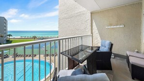 A balcony with a glass table, wicker furniture, and a view of a swimming pool and beach. - 410- Newly added 2 BR/ 2 BA Condominium with Free Beach Service! (Destin)