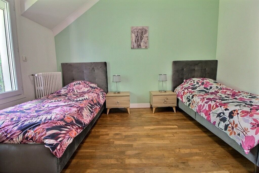 A bedroom with two single beds, a radiator, a window, and a wall-mounted picture.